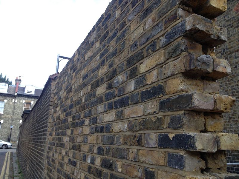 Tall garden wall built with reclaimed stock bricks and deep mortar joints