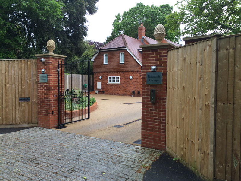 Cottage home with a red-tiled roof behind brick gate pillars and timber gates