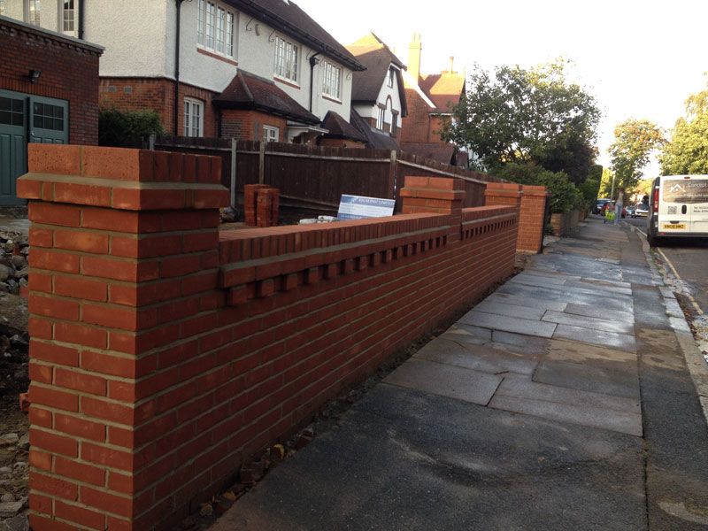 Newly built red-brick garden wall with piers and decorative brick detailing beside a street