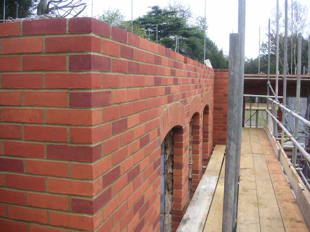 Red-brick garden wall with arched openings under construction