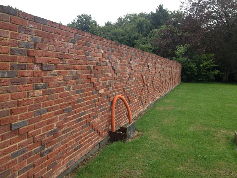 Long red-brick garden wall beside a lawn and trees
