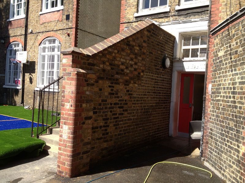 Stock-brick dividing wall with sloping brick coping beside a building entrance