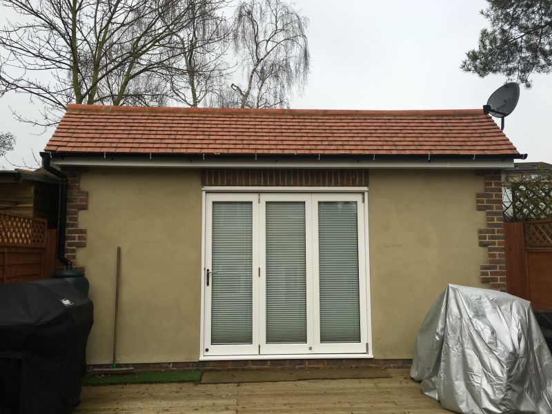 Rendered garden room with a tiled roof and white glazed doors onto a deck