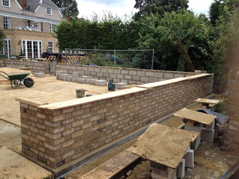 Long brick garden wall under construction with blockwork and protective capping boards