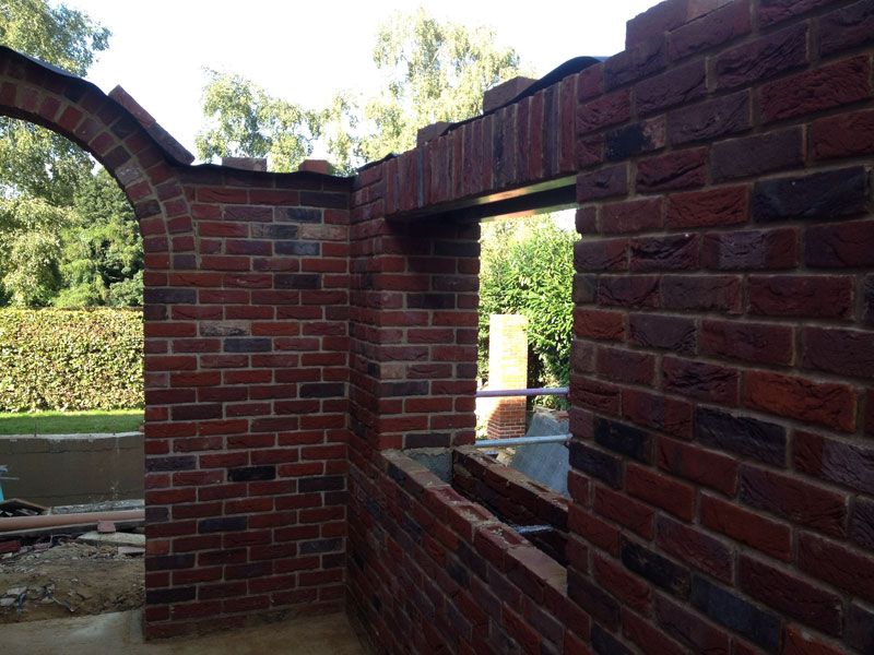 Red-brick arch and wall openings under construction in a garden