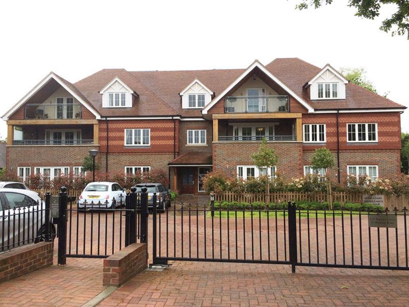 Red-brick residential apartment building with tiled roofs and balconies behind black gates